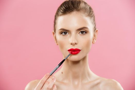 Beauty Concept - Woman applying red lipstick with pink studio background. Beautiful girl makes makeup.