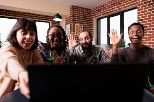 Multiracial people waving hand at online video conference on laptop while sitting at home. Diverse group of friends making greeting gesture at computer screen while on internet conversation.