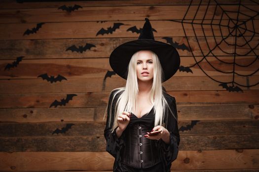 Halloween witch concept - Happy Halloween Sexy Witch holding posing with smartphone over old wooden studio background.