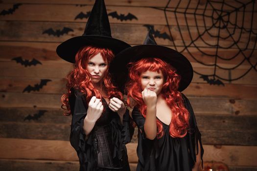 Halloween Concept - Beautiful caucasian mother and her daughter with long red hair in witch costumes witch cheerful fighting facial expression.