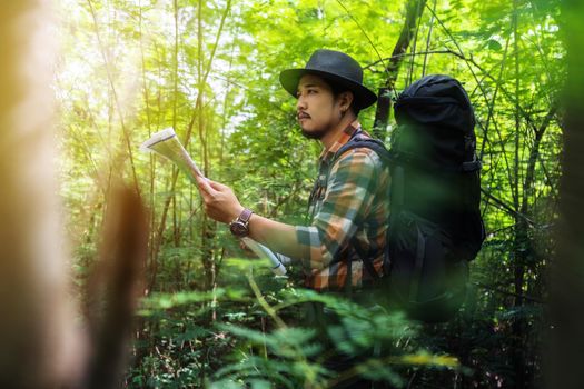 man traveler with backpack and map searching directions in the forest