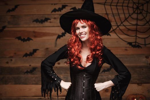 Halloween witch concept - Happy Halloween red hair Witch holding posing over old wooden studio background.