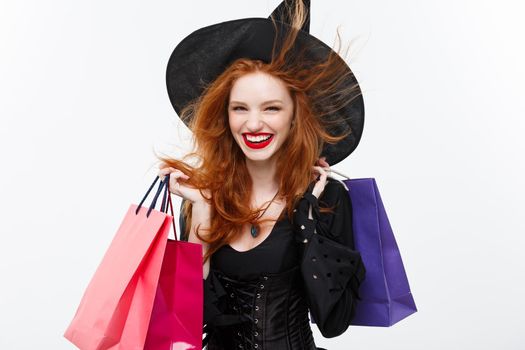 Halloween witch concept - Happy Halloween Witch smiling and holding colorful shopping bags on white background.