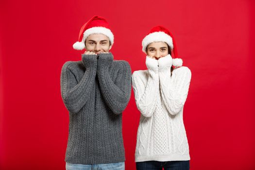 Christmas Concept - Portrait of smiling mouth tapping couple looking in camera with opened eyes over red studio background