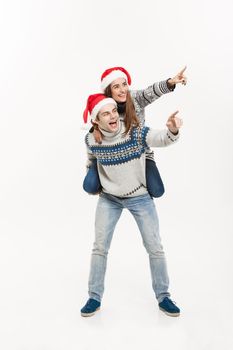 Christmas Concept - Full-length Young happy couple in sweaters enjoying piggyback ride isolated on white grey background