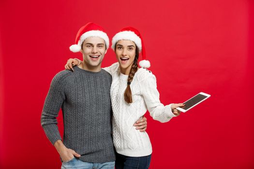 Christmas concept - Happy young couple in christmas sweaters holding digital tablet