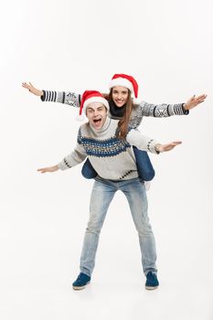 Christmas Concept - Full-length Young happy couple in sweaters enjoying piggyback ride isolated on white grey background