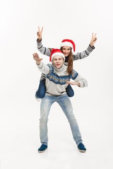 Christmas Concept - Young happy couple in sweaters enjoying piggyback ride isolated on white grey background