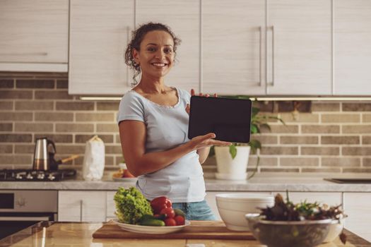 A woman watching or showing a video blog about cooking in her kitchen using tablet pc