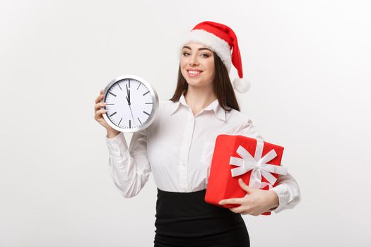 Time management concept - Young business woman with santa hat holding a clock and present isolated over white background.
