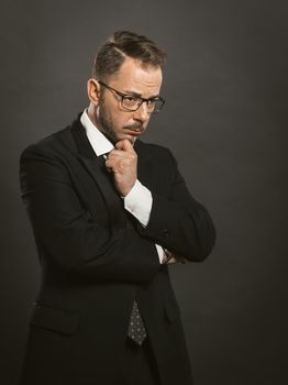 Doubting businessman crossed his arms touching his chin. Thoughtful intelligent man in glasses stands hesitantly looking to the side. Doubt concept. Toned image