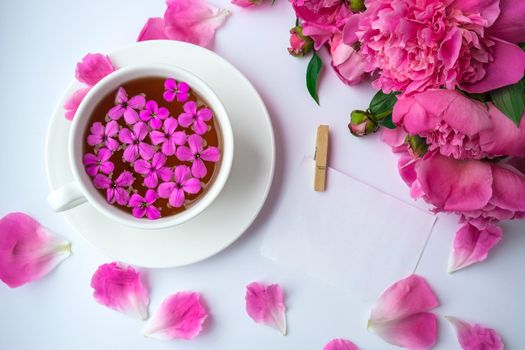 Creative layout with pink peonies flowers and cup of tea on bright table. Paper note. Copy space. Spring Seasonal valentine, woman, mother, 8 march holiday, romance breakfast. Stylish blogger. Greeting card