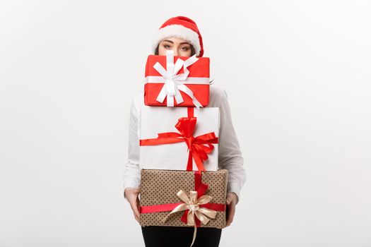 Business Concept - Beautiful young caucasian business woman with santa hat hiding behide a lot of christmas gift boxes with copy space on side.