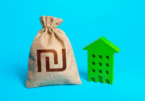 Israeli shekel money bag and green resident building. Investment in green technologies. Reduced emissions and improved energy efficiency. Reducing impact on environment. Sustainable housing.