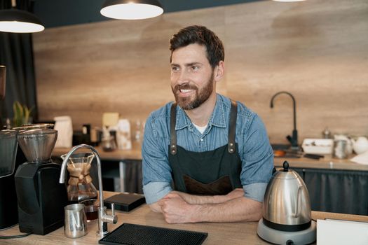 Positive barista standing behind counter and waiting for a client
