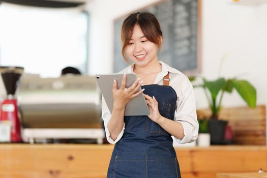 Portrait of Asian Barista cafe owner with tablet to check order. SME entrepreneur seller business concept.