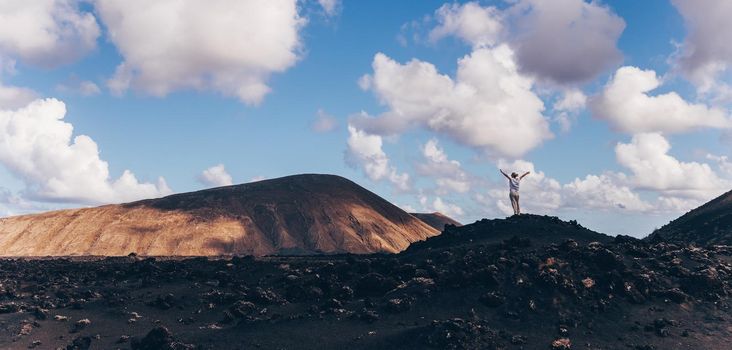Woman rising hands up in the sky, enjoying amazing views of volcanic landscape in Timanfaya national park on Lanzarote, Spain. Freedom and travel adventure concept.