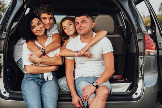 Portrait of Happy Four Caucasian Members Family Sitting in Trunk of Minivan Car, Mother and Father with Two Teenage Children, Son and Daughter Having Weekend Outdoors