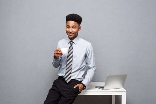Business Concept - portrait of african american businessman having coffee sitting at a desk using a laptop
