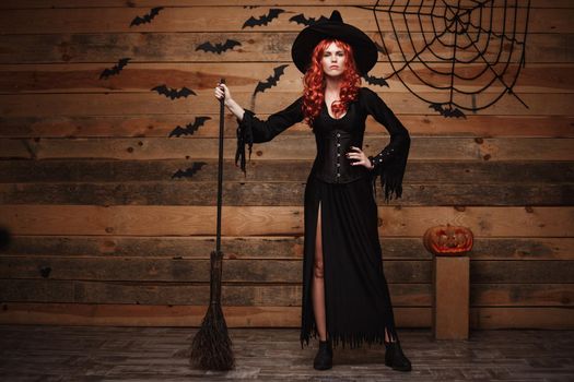 Halloween witch concept - Full-length Happy Halloween red hair Witch holding posing with magic broomstick over old wooden studio background.