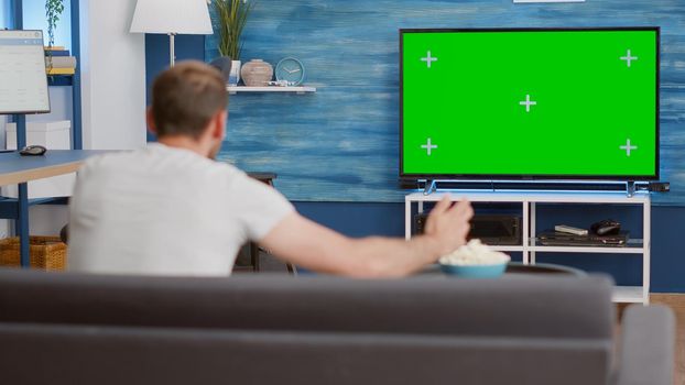 Sports fan watching game on green screen tv mockup encouraging favourite team while relaxing at home