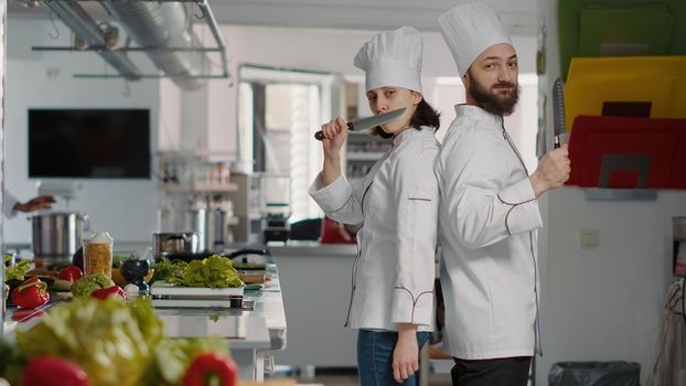 Portrait of chefs team acting funny with knives in restaurant kitchen