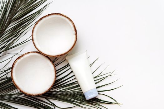 Skin care cream with coconut oil on a white background with palm leaves and coconuts. Body and hair treatment concept.
