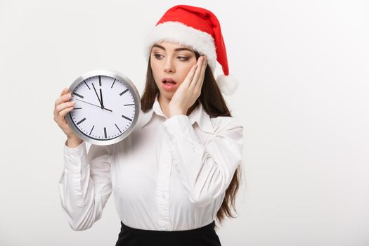 Time management concept - Young business woman with santa hat holding a clock isolated over white background.