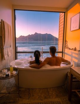 man and woman in bath tub jaccuzi on vacation, couple man and woman in bath tub looking out over the ocean of Cape Town South Africa during vacation
