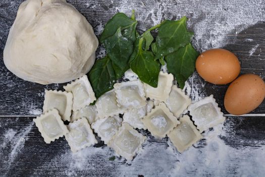 dough with spinach eggs, flour and ravioli on wood
