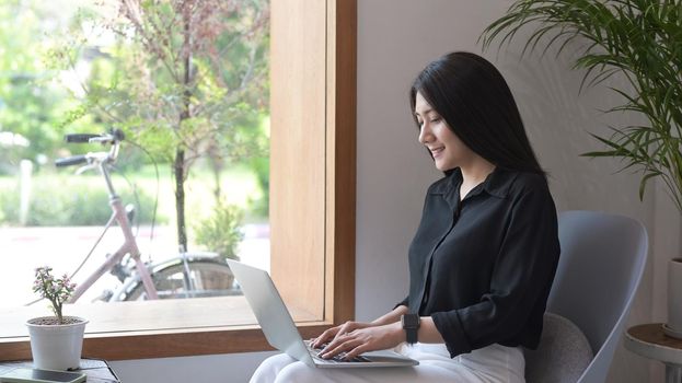 Attractive asian woman sitting in contemporary coffee shop and using laptop computer