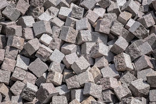 Pile of natural stone cubes for making outdoor pavement tiles. Chaotic stack of road tiles. Stone blocks.