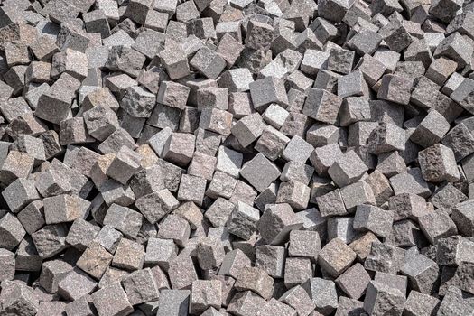 Pile of natural stone cubes for making outdoor pavement tiles. Chaotic stack of road tiles. Stone blocks.