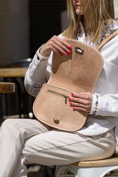 woman holds small beige women's leather bag with a carved pattern. selective focus