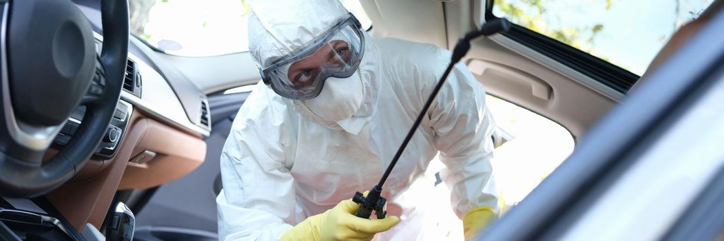 A specialist in a protective suit disinfects the car