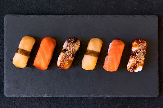 Assorted sushi with salmon, eel and escolar on black stone plate on dark background. Minimal concept