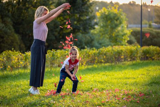 Mom plays with her daughter in the park, sprinkles autumn leaves on top. Russia Moscow September 24, 2020