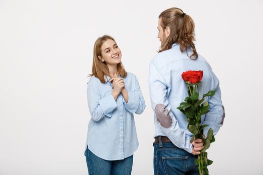 Portrait of handsome elegant guy is surprising his beautiful girlfriend with red roses and smiling over white isolated background.