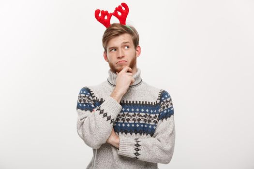 Holiday Concept - Young beard man in sweater with thoughtful gesture on white background.