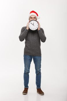 Holiday concept - Young handsome beard man hidden behind white clock over white studio background.