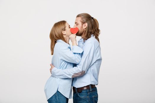 Young attractive couple in blue shirt holding paper heart and kissing.