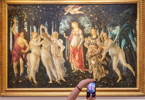 Florence, Italy - circa July 2021. Turist taking picture of Botticelli - Spring. Caucasia woman hands with mobile