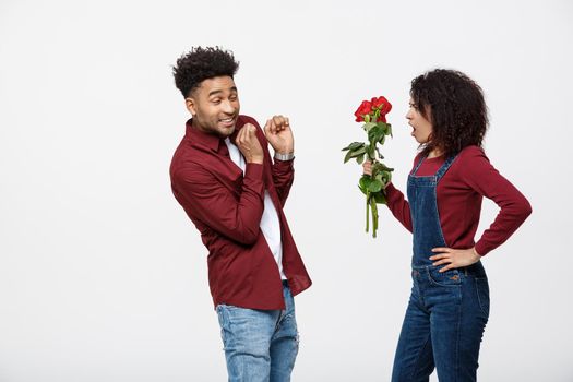 Portrait of a disappointed young woman holding red rose with while standing and angry on her boyfriend isolated over white background