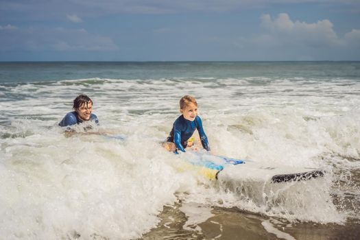 Father or instructor teaching his 5 year old son how to surf in the sea on vacation or holiday. Travel and sports with children concept. Surfing lesson for kids