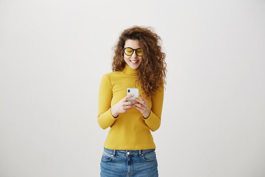 Image of gorgeous woman in casual being surprised or excited to receive pleasant text message on her cell phone, over gray background.