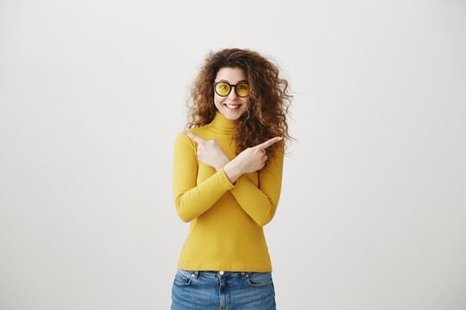 Excited young woman pointing her finger towards blank space isolated over grey background.