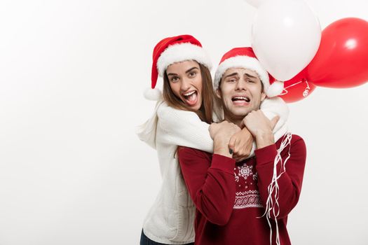 Christmas Concept - Young girlfriend holding balloon is hugging and playing with her boyfriend doing a surprise on Christmas