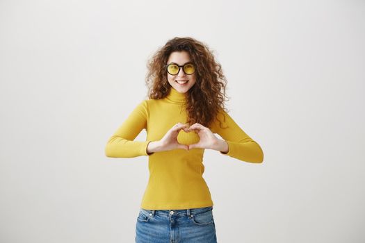 Cheerful beautiful girl making heart by hands isolated on a gray background.