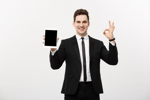 Business Concept: Cheerful businessman in smart suit with pc tablet showing ok. Isolated over grey background.
