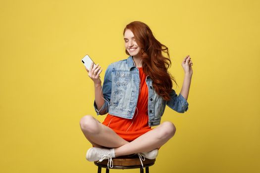 Lifestyle, Music, Technology concept: Young beautiful caucasian woman listening music with headphones and smart phone hand hold, dancing, eyes closed smiling, Isolated on yellow vivid background.